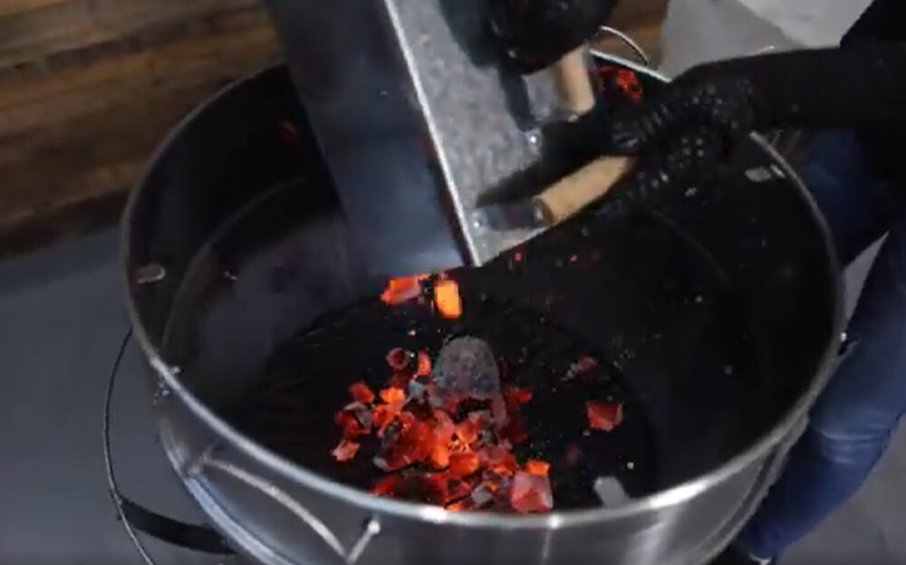 This image shows the lit charcoal being place in the kettle rotisserie