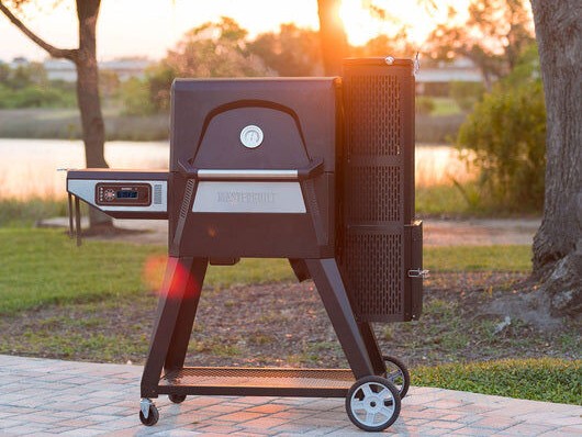 Masterbuilt Gravity Series 560 Digital Charcoal Grill & Smoker outdoors at sunset, showing its digital control panel and vertical charcoal hopper.