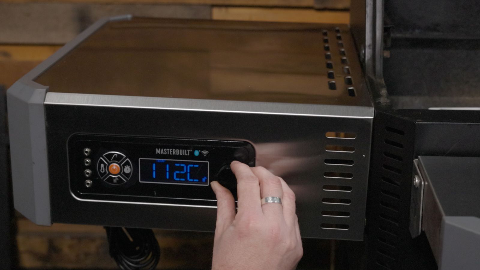 Adjusting digital control dial on a Masterbuilt Gravity Feed Smoker set to 112°C for precise BBQ cooking.