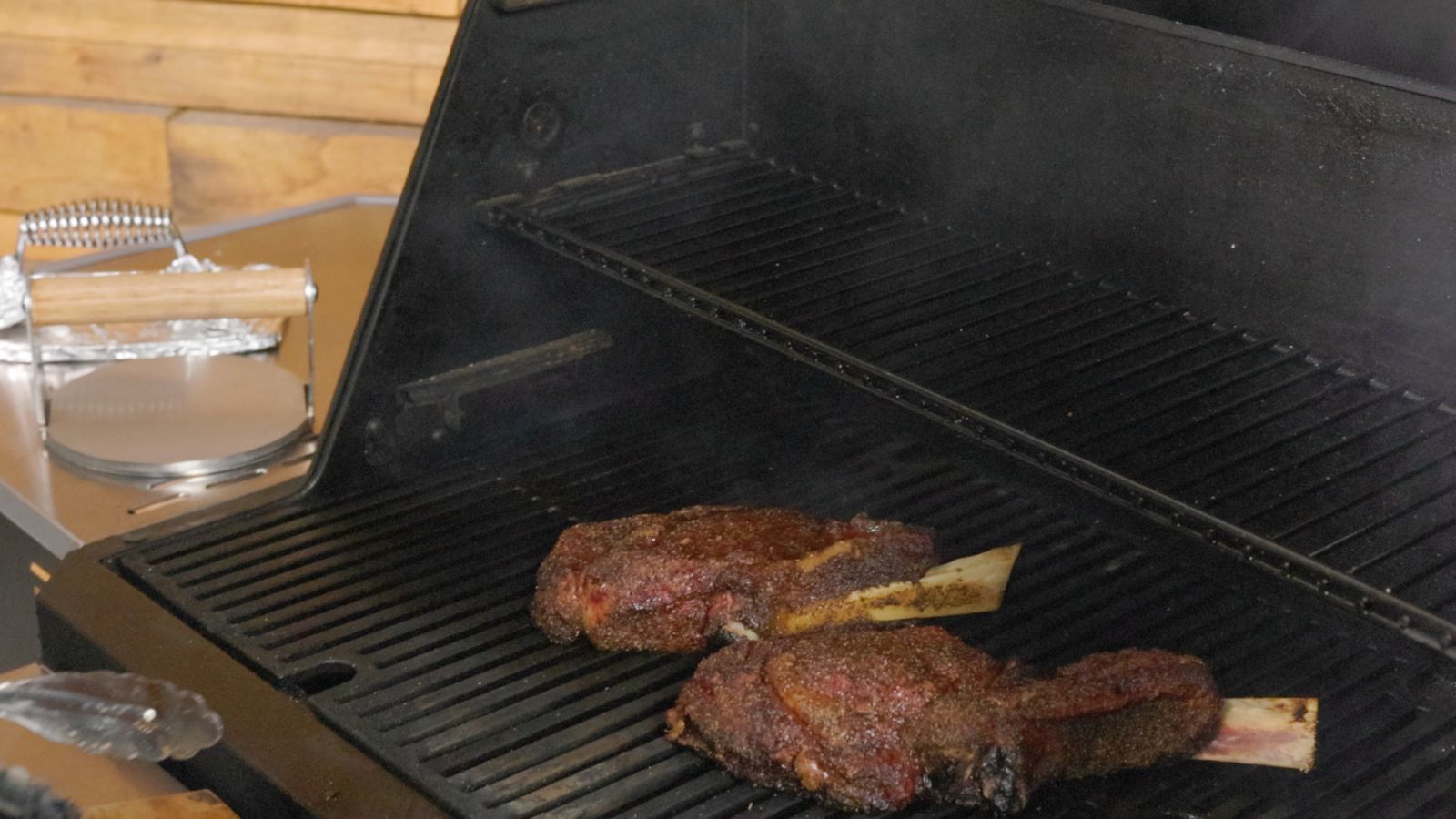 Two seasoned tomahawk steaks searing on a Masterbuilt Gravity Feed Smoker grill grates.