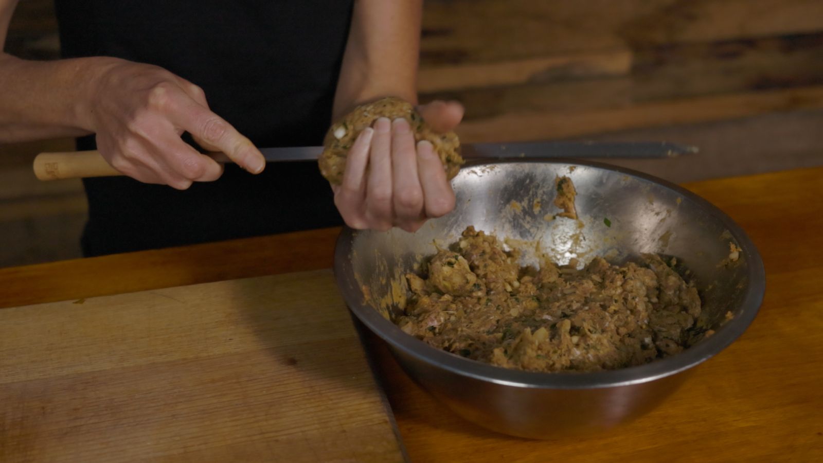 Person shaping seasoned minced meat onto a flat skewer by hand, with a large metal bowl of kebab mixture on the table beside them.