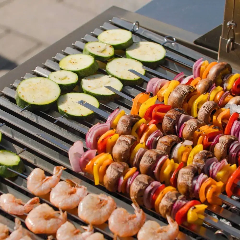 Vegetables, mushroom skewers and prawns cooking over a parrilla grill with charcoal heat.