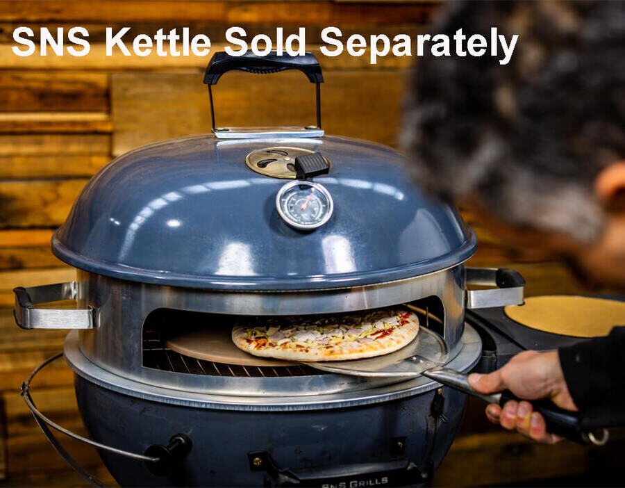 A person slides a pizza into an SNS Kettle Pizza Attachment fitted on a charcoal kettle grill. The setup transforms the BBQ into a pizza oven, with the thermometer on the lid showing precise temperature control for perfect wood-fired pizza cooking.