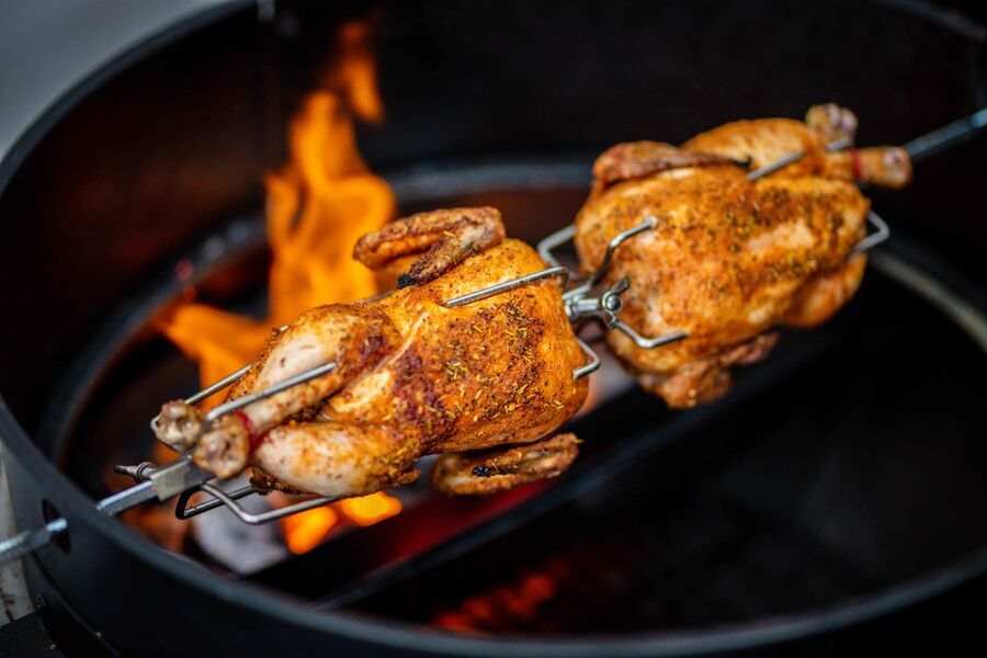 Double ended rotisserie fork holding whole chickens cooking over charcoal