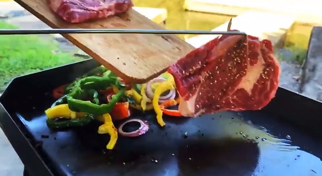 This image shows the Pig Tail BBQ flipper grapping a piece of stake as it is being placed on a BBQ