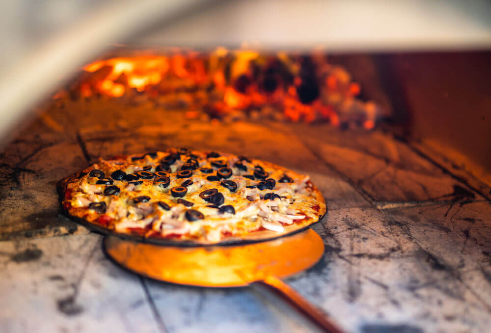 This image shows a pizza being cooked in the Wood Fired Pizza Oven