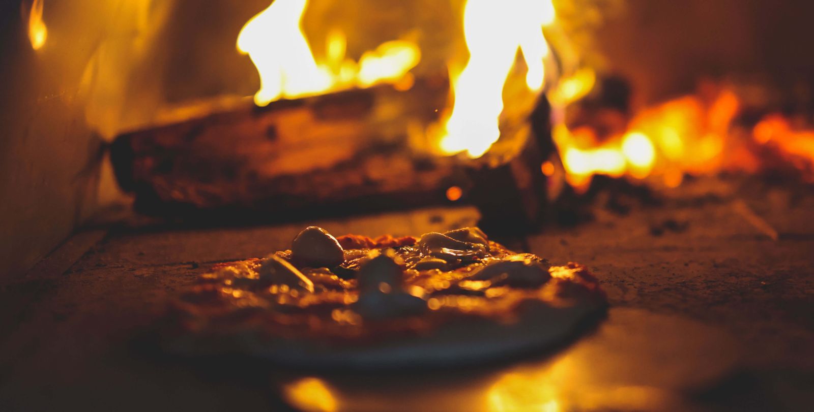 This image shows delicious pizza being placed in the Wood Fired Pizza Oven