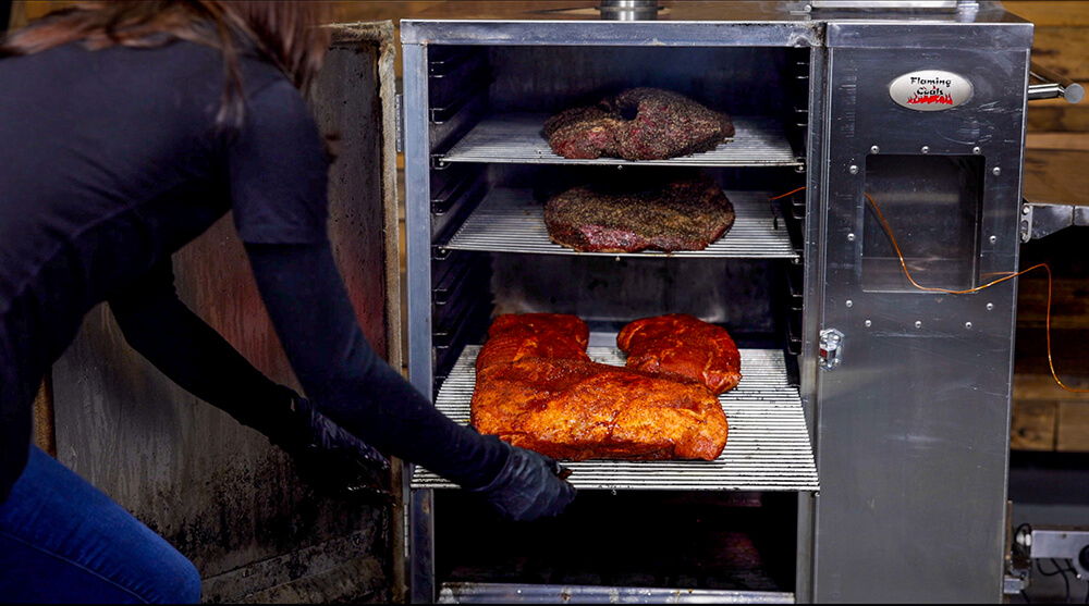 This image shows pork shoulder being placed in the Flaming Coals Offset Smoker 