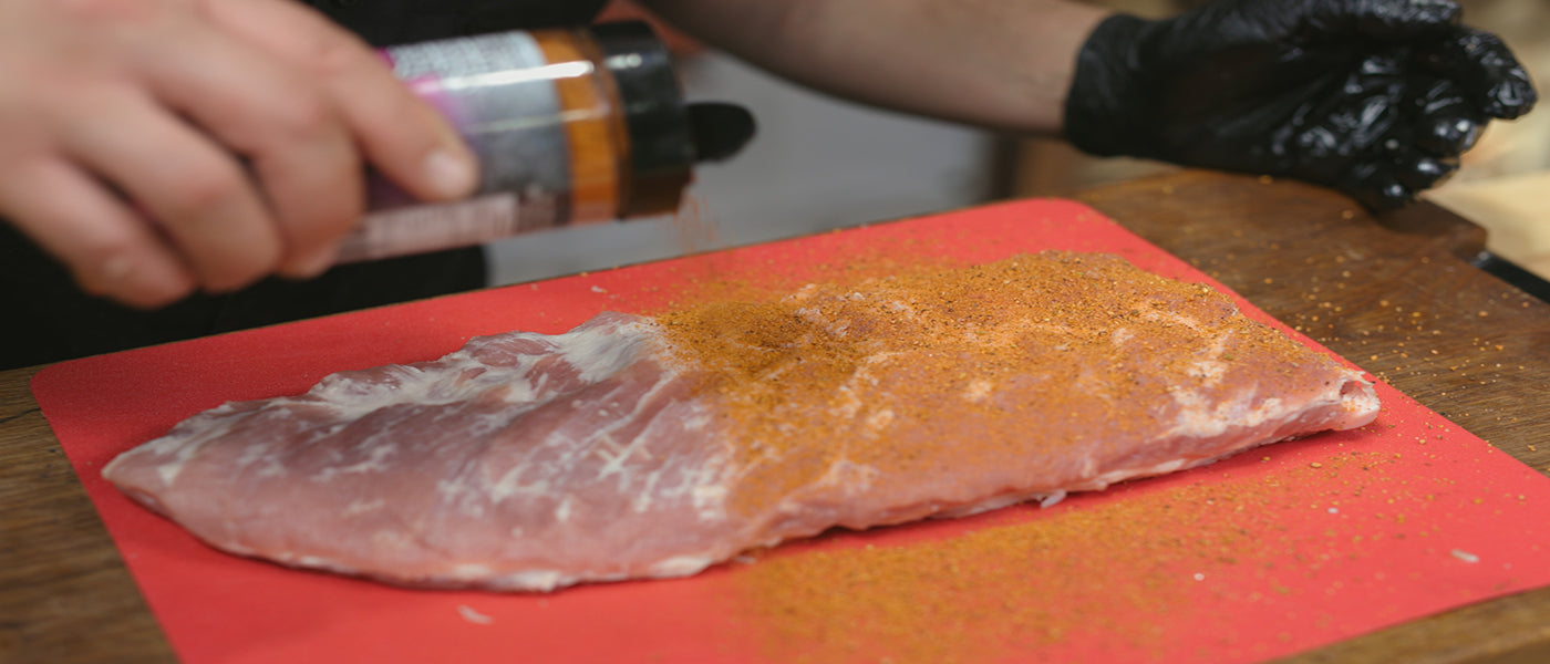 This image shows a man seasoning the pork Ribs with Slow burner Bbq power house Rub