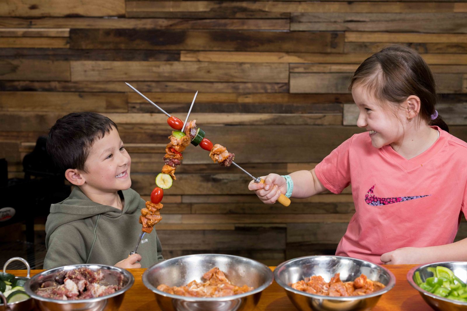 Kids enjoying BBQ prep with skewers of chicken, pork, and vegetables, highlighting family fun and outdoor cooking with Flaming Coals seasonings.