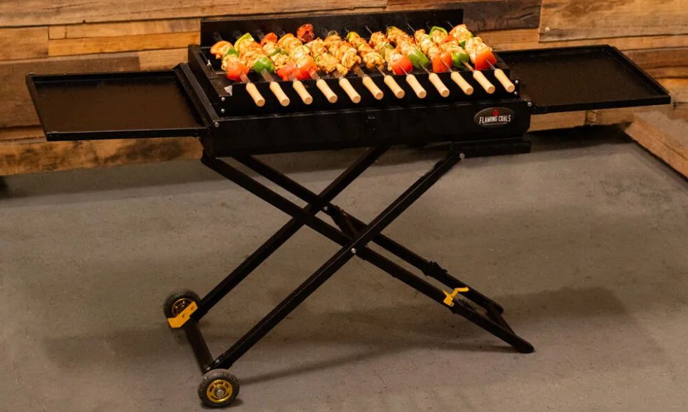 Portable foldable charcoal shashlik grill cooking skewers of chicken and vegetables on raised skewer rack.