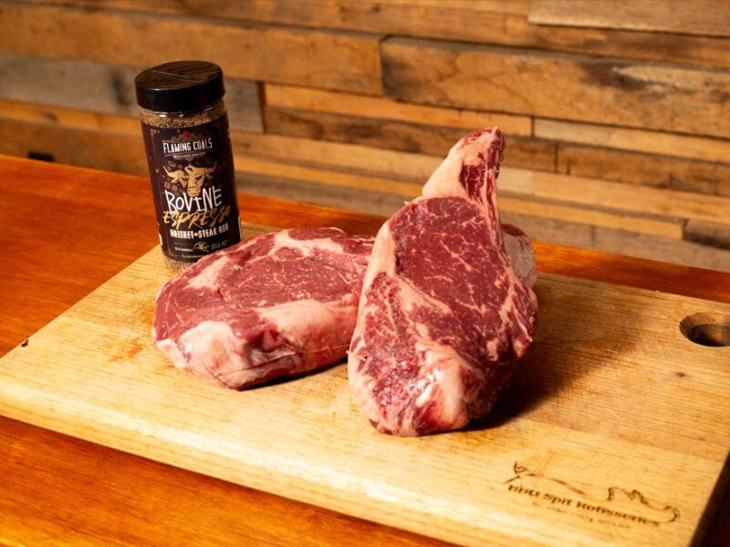Raw ribeye steaks on a wooden board with  Espresso brisket and steak rub seasoning.