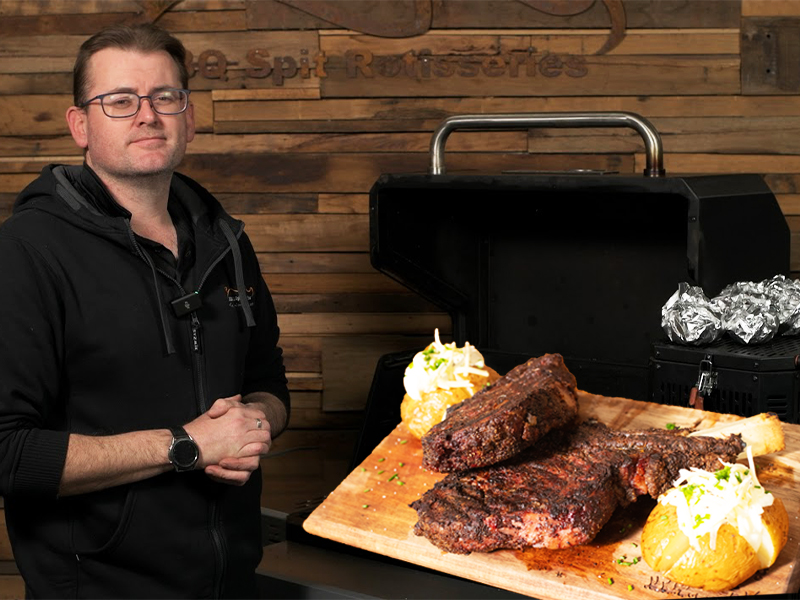 Reverse sear steaks and baked potatoes cooked on a Masterbuilt Gravity Feed Smoker, served on a wooden board with sour cream and chives.