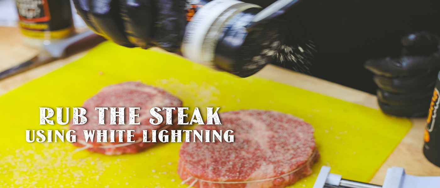 This image shows a man seasoning the steak using the White Lightning Rub