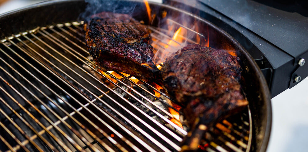 Steak cooking on an SNS grill with water reservoir and charcoal baskets, flames rising to create the perfect smoke flavour.