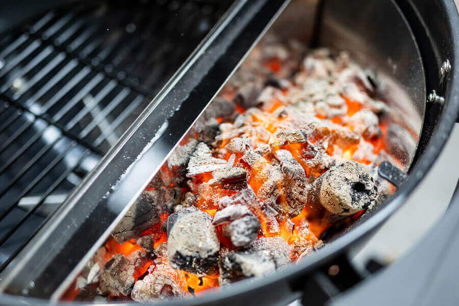 Slow N Sear Deluxe Charcoal Basket inside a Weber Kettle Grill, filled with glowing hot coals for high heat cooking.