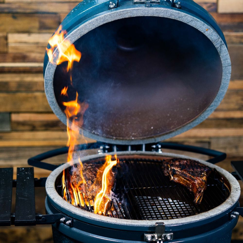 Slow ’N Sear Kamado Grill with the lid open, flames searing steaks over charcoal on cast iron grates.