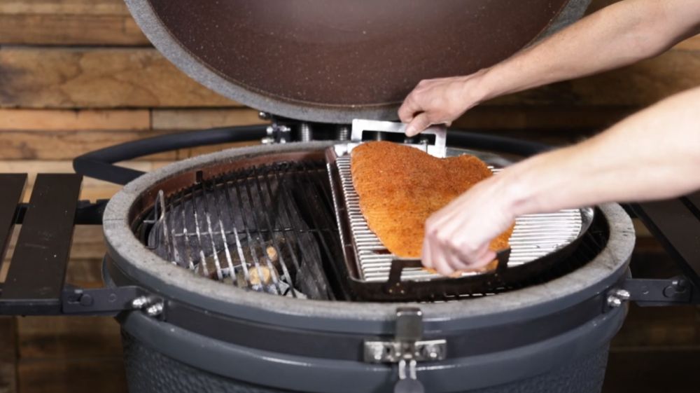 Person placing a seasoned salmon fillet onto the grill inside an SNS Kamado, preparing it for smoking and slow cooking over charcoal.