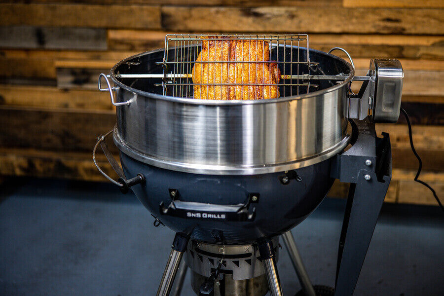 Rotisserie chicken cooking on a kettle BBQ with a stainless steel rotisserie ring attachment and motorized spit setup.