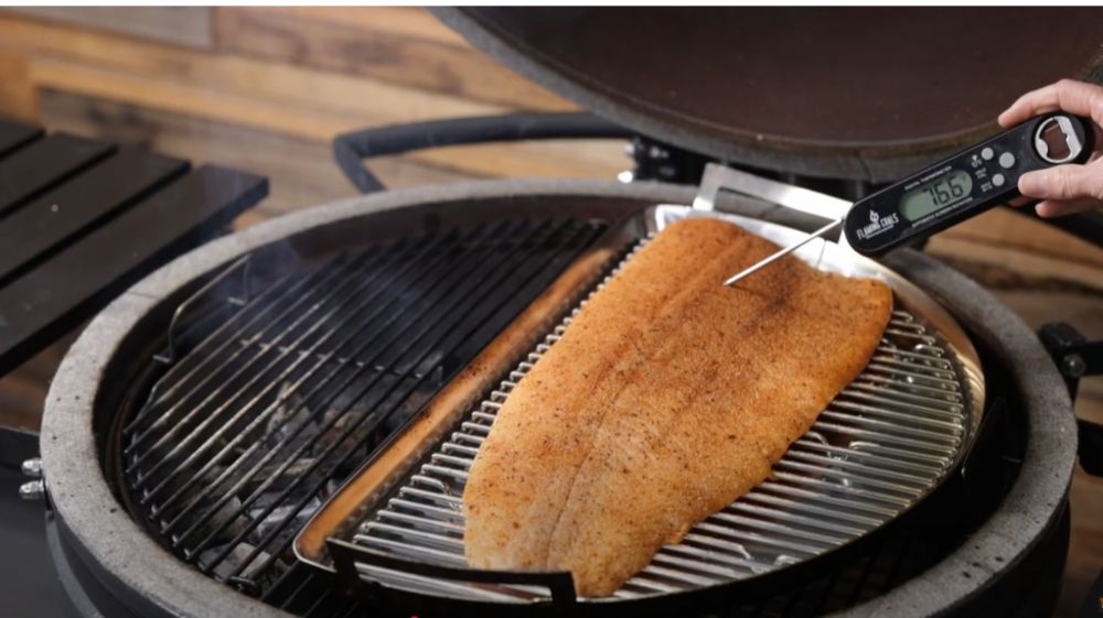 Person checking the internal temperature of a seasoned salmon fillet using a digital meat thermometer on the SNS Kamado, ensuring it reaches the perfect cook