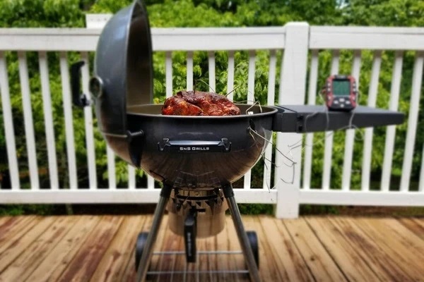 This is an image of sns Grills, slow n sear kettle BBQ, on a patio cooking meat with a remote thermometer plugged in. This is a great quality alternative to a weber kettle and even better with the slow n sear accessory 