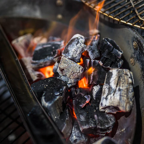 Glowing charcoal burning in the SNS grill charcoal basket, creating steady heat and smoke for perfect BBQ cooking.
