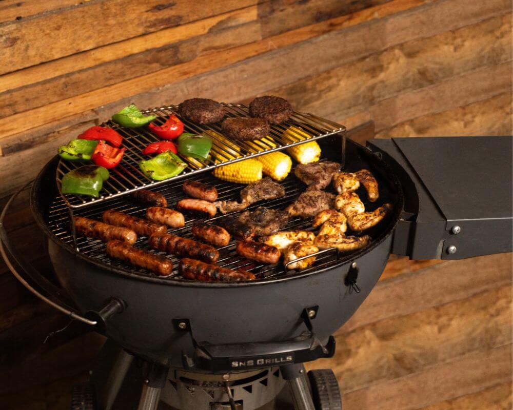 Slow ‘N Sear Kettle BBQ loaded with sausages, chicken wings, lamb chops, corn on the cob, burger patties, and grilled capsicum for a backyard feast.