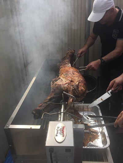 Picture of men carving a lamb that was cooked on a charcoal rotisserie