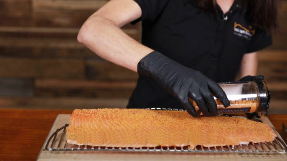 Person seasoning a fresh salmon fillet with Flaming Coals Gyros Rub, preparing it for a flavourful grilling session.