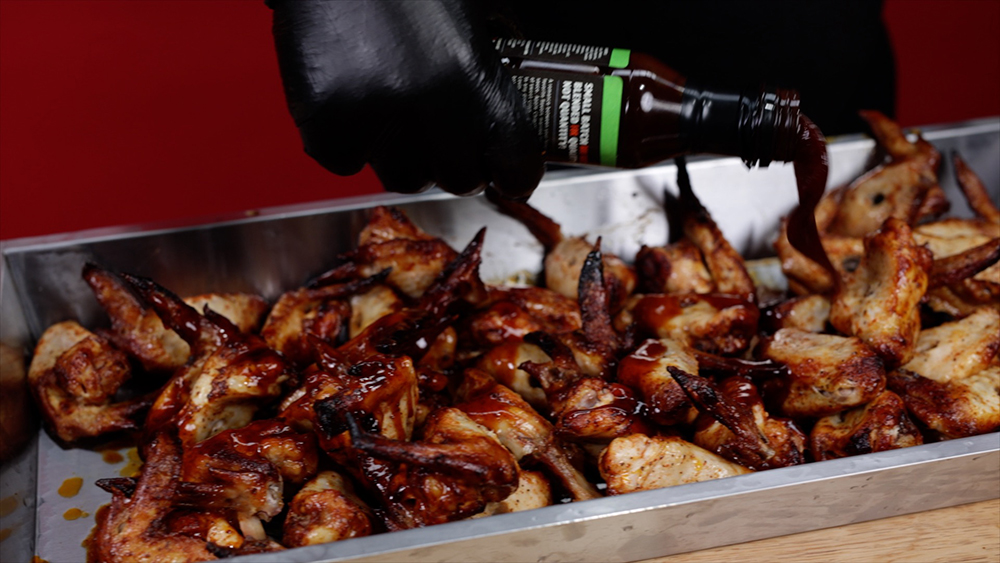 This image shows chicken wings being seasoned with Kosmos Q Apple Chipotle Sauce