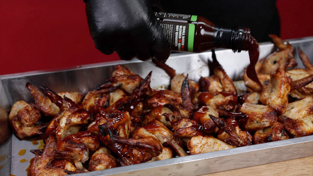 This image shows chicken wings being seasoned with Kosmos Q Apple Chipotle Sauce