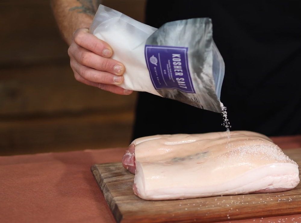 This image shows pork belly being seasoned with kosher Salt