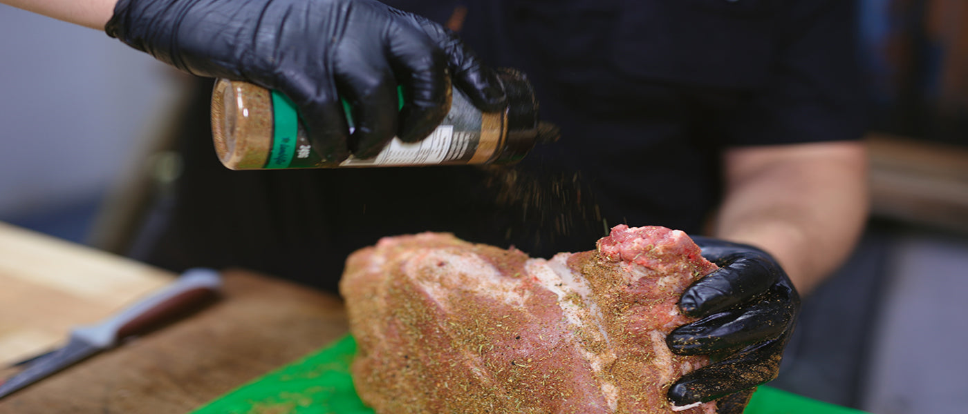 This image shows a man seasoning the lamb shoulder with Slow Burner bbq Rub