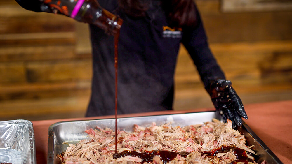 This image shows pulled pork being seasoned with Kosmos Q Raspberry Chipotle 