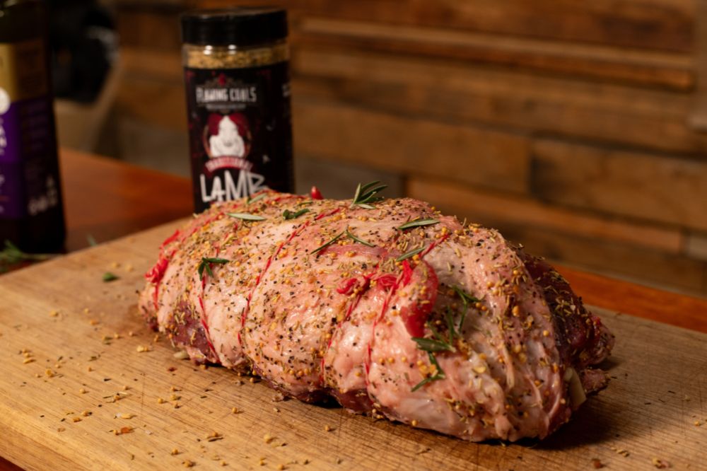 Boneless lamb roast seasoned with Flaming Coals Lamb Rub and fresh rosemary, tied with butcher’s twine and ready for cooking on a wooden cutting board.