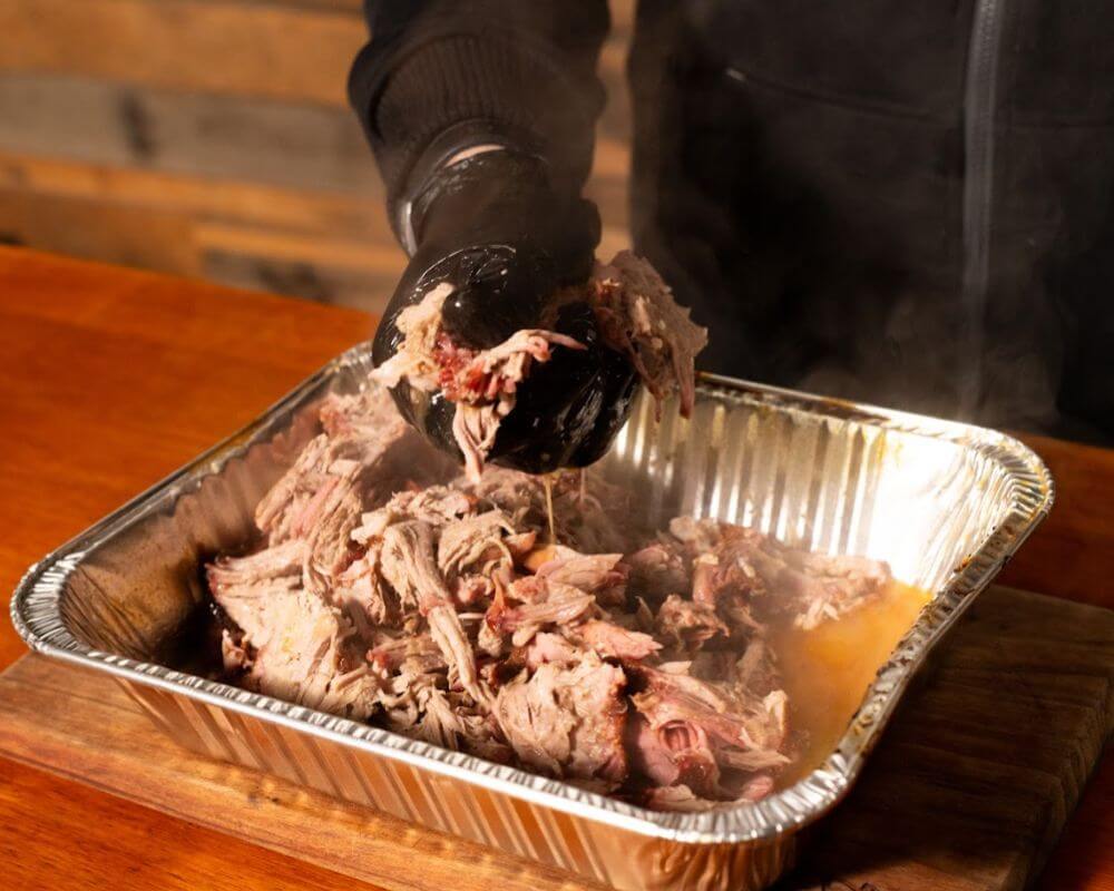 Shredding smoked pulled pork in a foil tray after cooking on a Masterbuilt Gravity Feed Smoker.