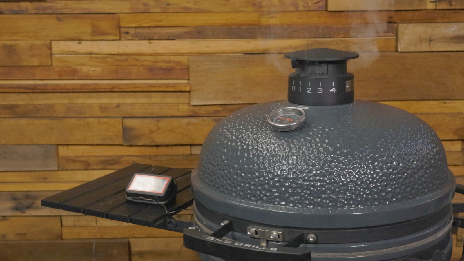 SNS Kamado grill with a thermometer and smoke vent visible, sitting against a wooden background.