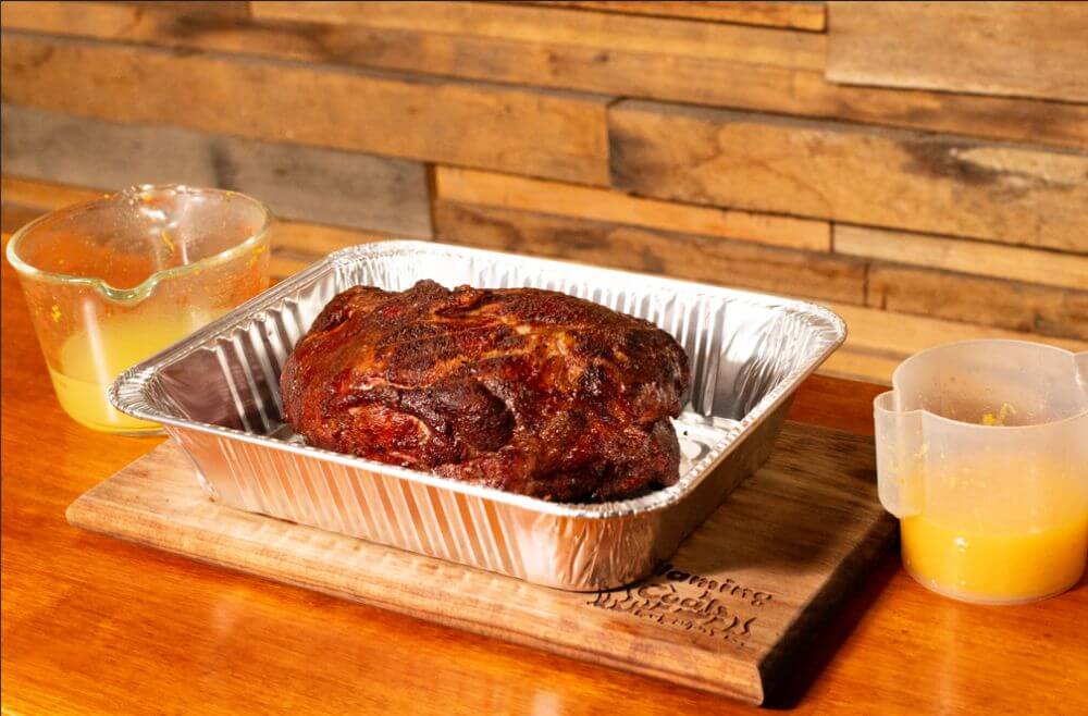 Smoked pork shoulder after 3 hours in the Masterbuilt Gravity Feed Smoker, resting in a foil tray with orange juice.