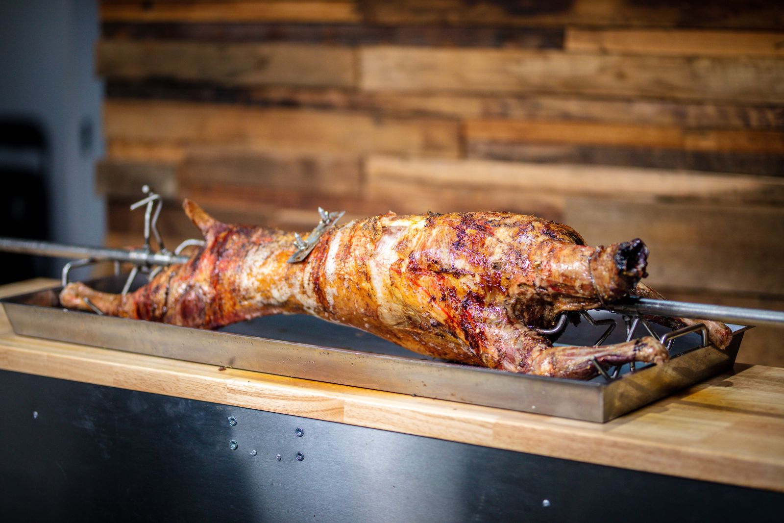 Whole spit-roasted lamb placed on a stainless steel carving tray, showing golden crispy skin and carving readiness.
