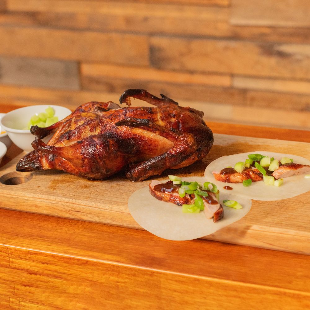 Spit roasted duck cooked on a Masterbuilt Smoker using a Spit Rotisserie kit, served on a wooden board with sliced portions in wraps topped with spring onions.