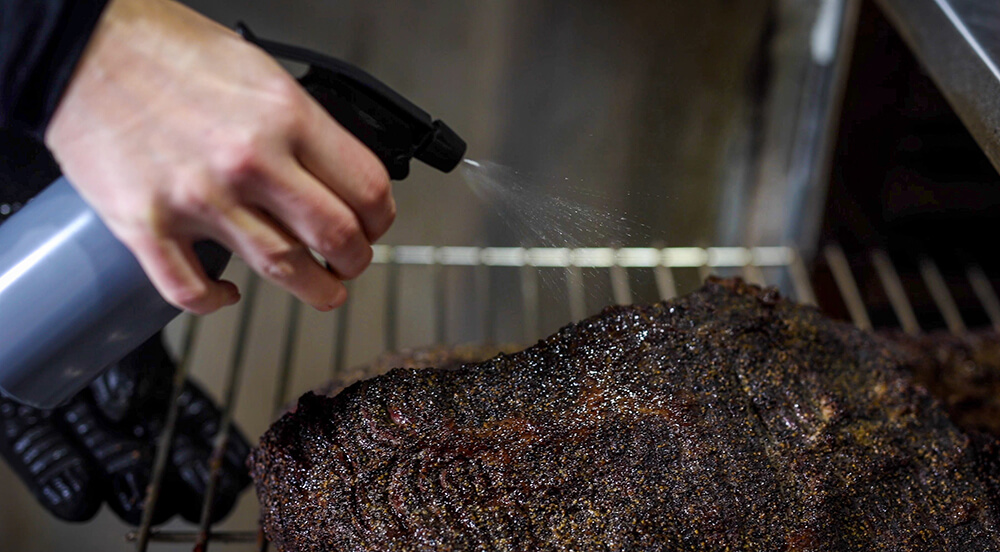 This image shows spritzing the brisket in the Flaming Coals Offset Smoker