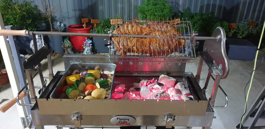 Stainless steel Cyprus spit roasting whole meat over glowing charcoal with vegetables cooking alongside.
