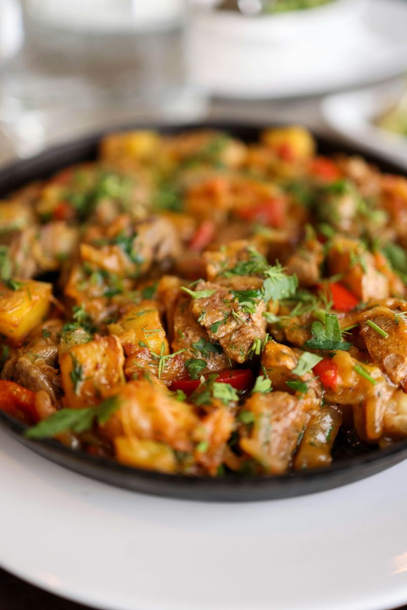 Close-up of a sizzling pan of spiced meat stew with potatoes, peppers, and fresh herbs served hot on a plate. Photo by pexels-valeriya-20350160