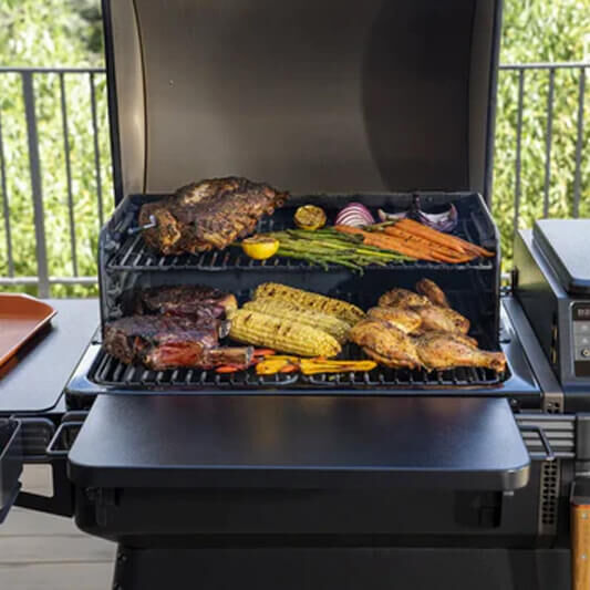 Pellet grill loaded with ribs, chicken, corn, and vegetables.