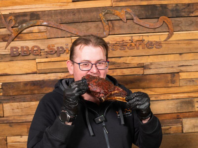 Cameron enjoying a taste test of reverse sear tomahawk steak cooked on a Masterbuilt smoker at BBQ Spit Rotisseries.
