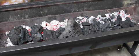 This_image_shows_how_charcoal_is-added_to_a_spit_roaster_during_a_cook