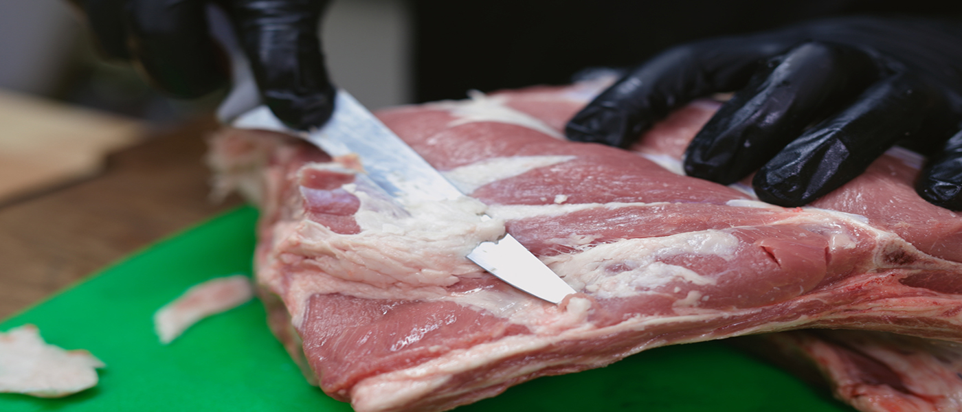 This image shows a man trimming the fats of lamb shoulder