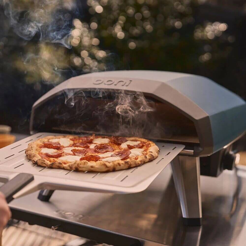 Ooni Koda 2 gas pizza oven cooking a freshly baked pizza on a perforated peel with steam rising