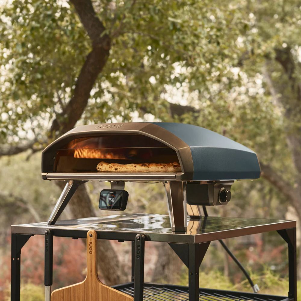 Ooni Koda 2 Pro gas pizza oven cooking a pizza outdoors on a stainless steel prep table with digital temperature display