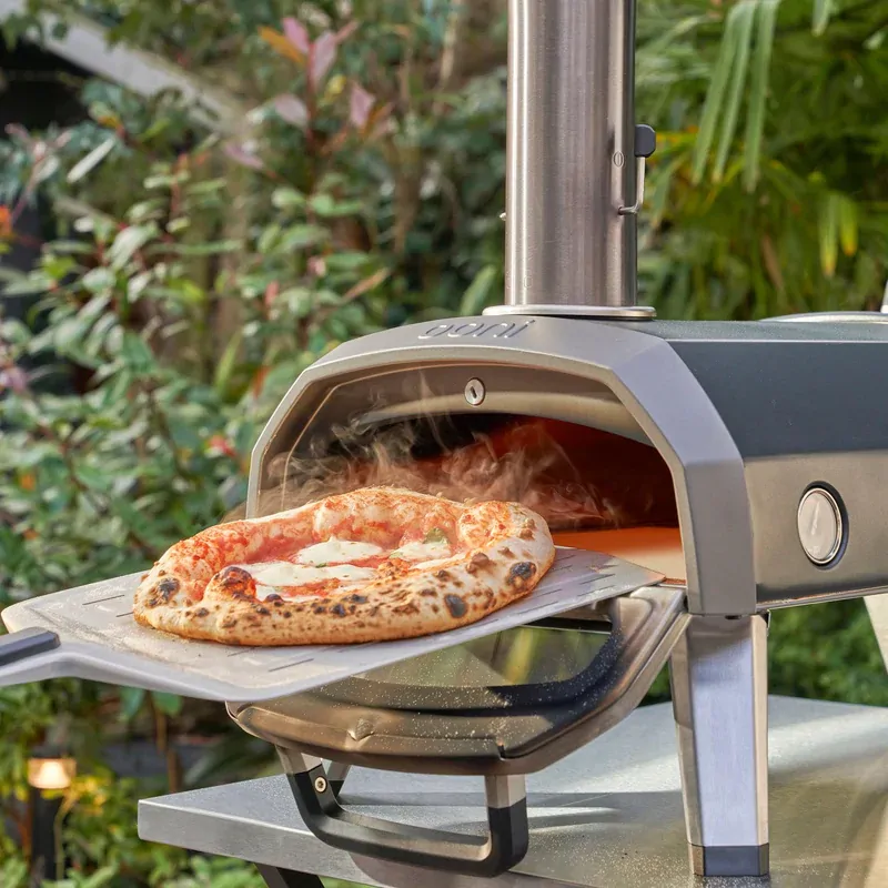 Ooni Karu 2 multi fuel pizza oven cooking a wood fired pizza outdoors with rotating pizza stone and chimney attached.